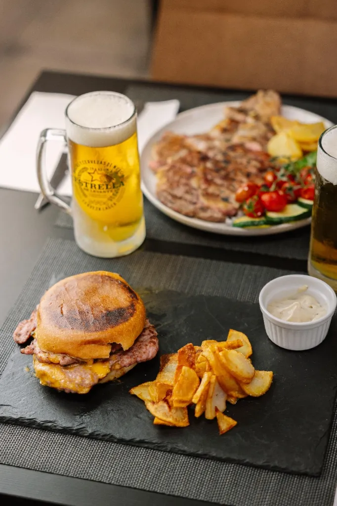 Mesa servida con hamburguesas, entrecot y cervezas en El Bessó